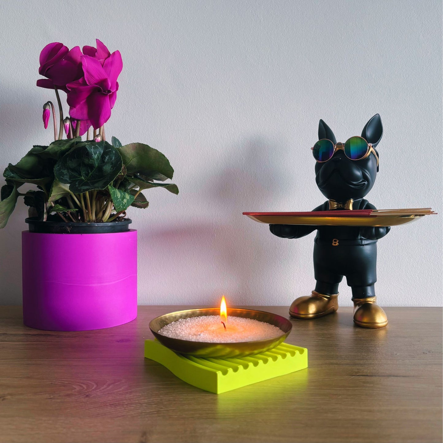 Decorative scene with a potted plant, candle, and figurine on a wooden surface.