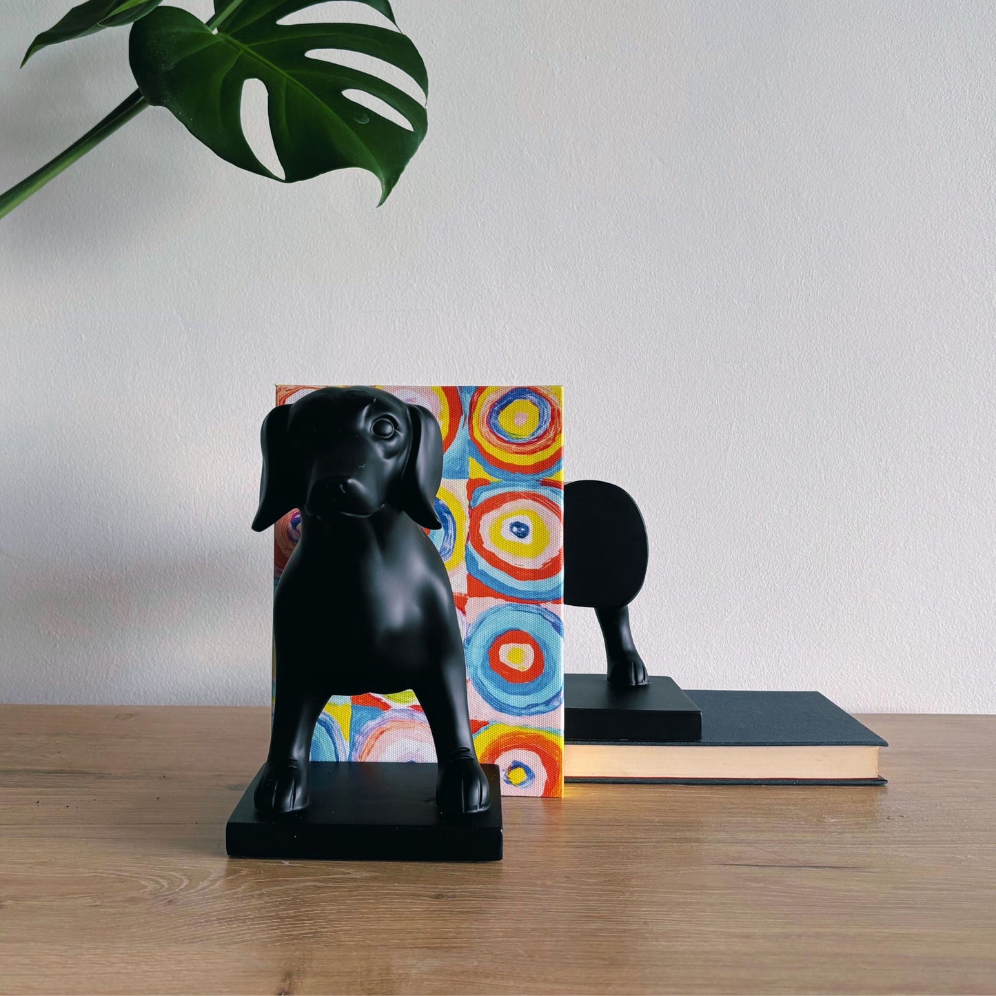 Black dog-shaped bookends on a wooden surface with a colorful book and plant in the background.