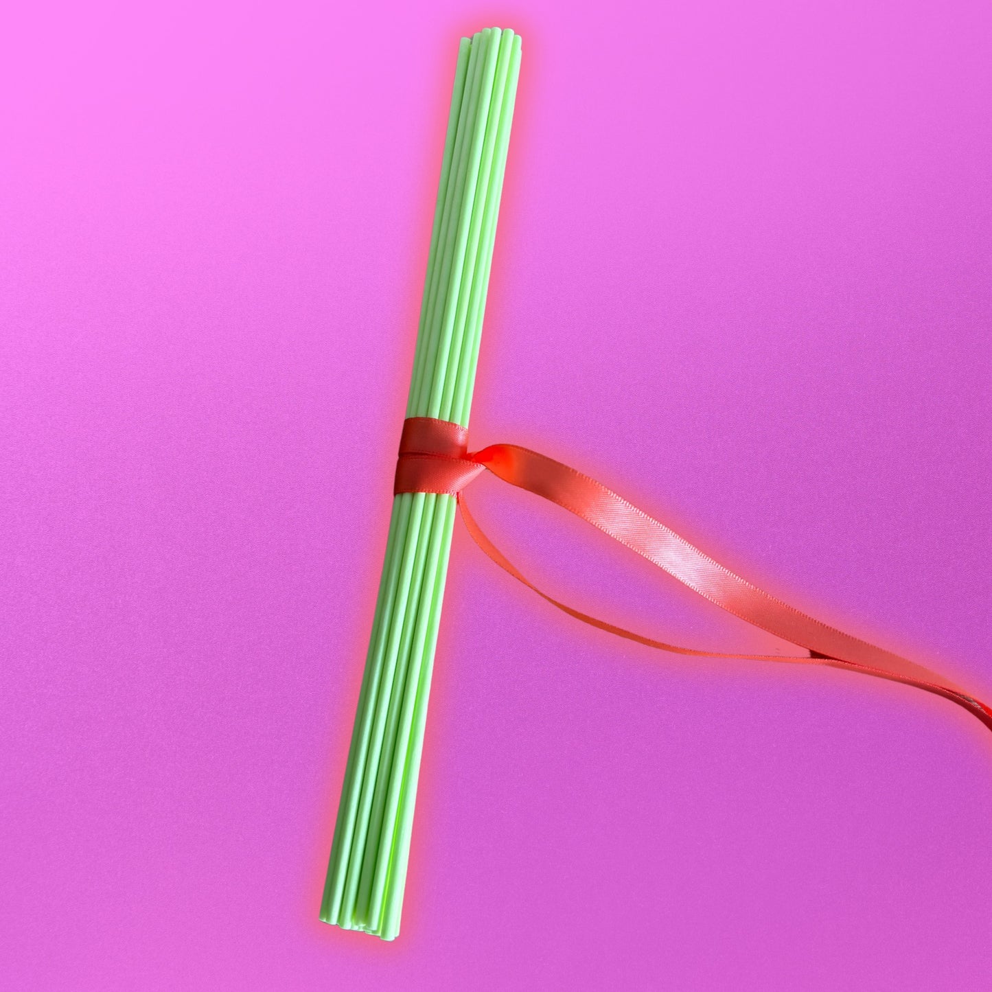 Green diffuser reeds with a red ribbon on a pink background