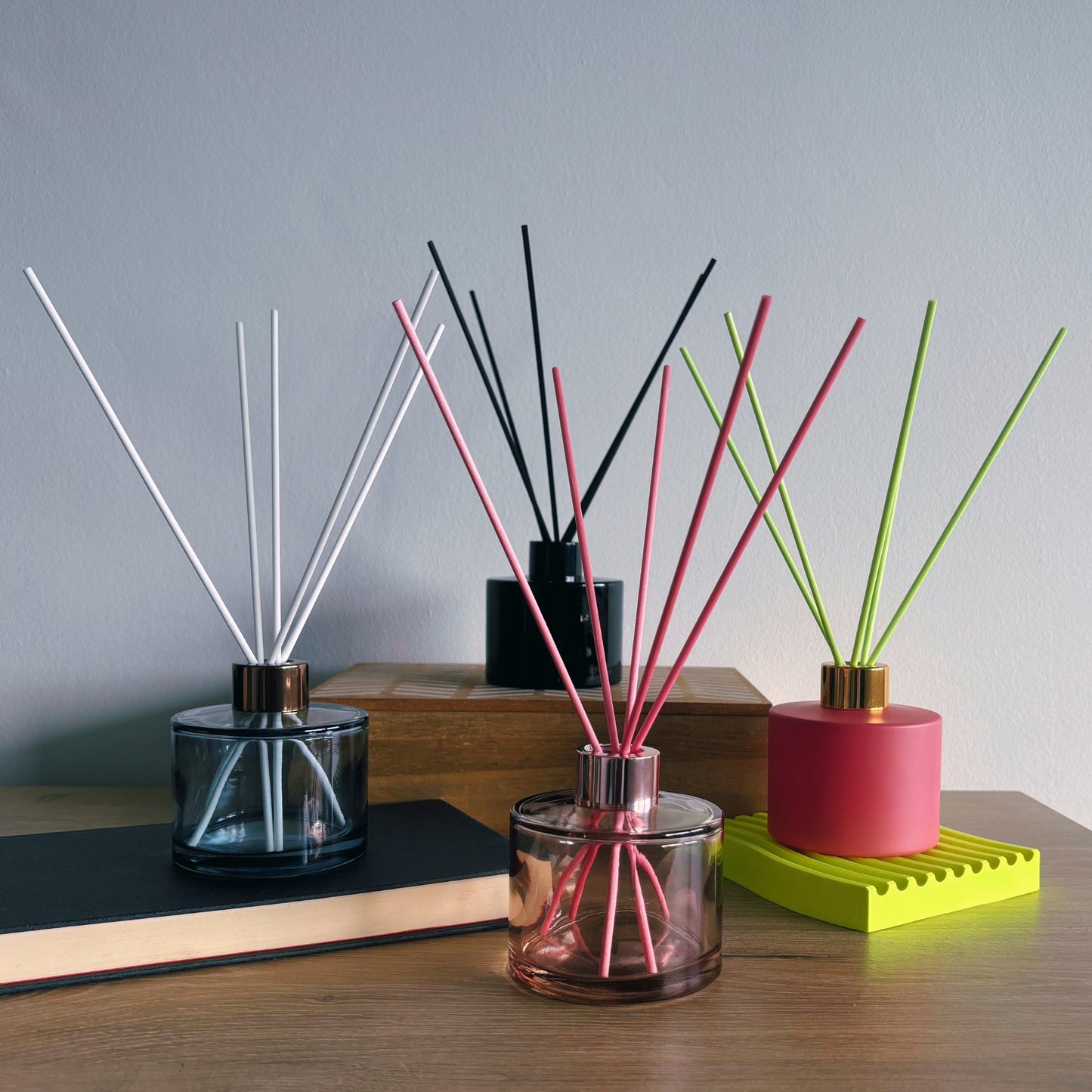 Three diffusers with sticks in different colored containers on a wooden surface.