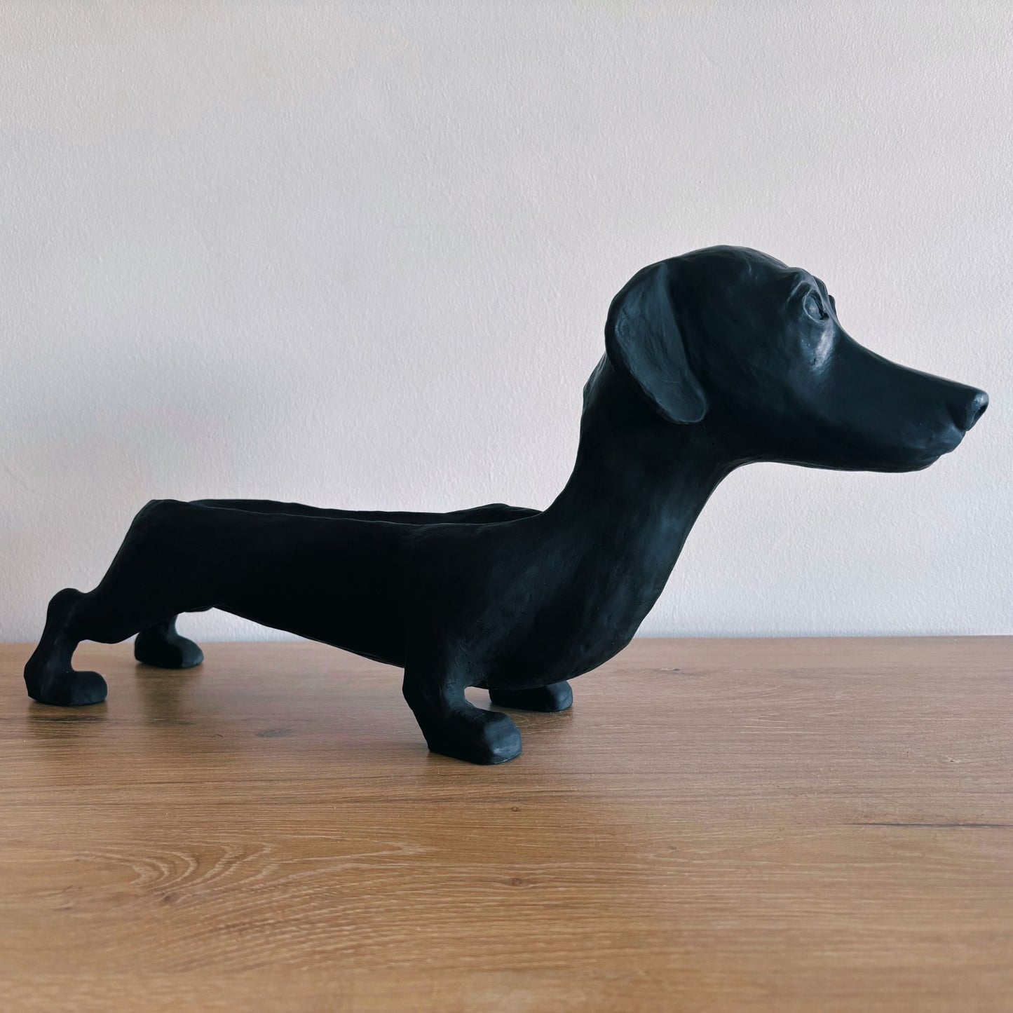 Black dachshund-shaped object on a wooden surface with a plain background