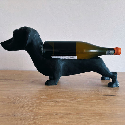 Black dog-shaped wine bottle holder with a wine bottle on a wooden surface.