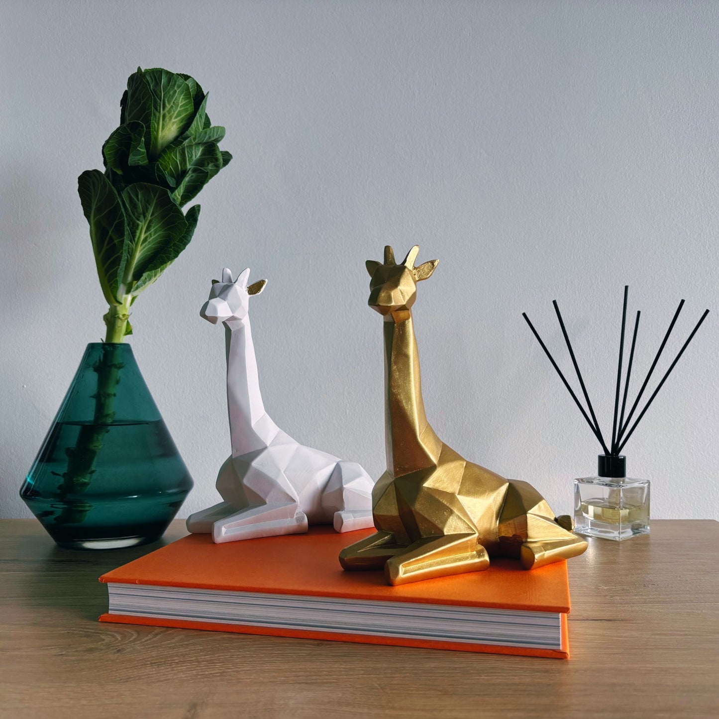 Decorative giraffe statues on an orange book with a green vase and black diffuser in the background.