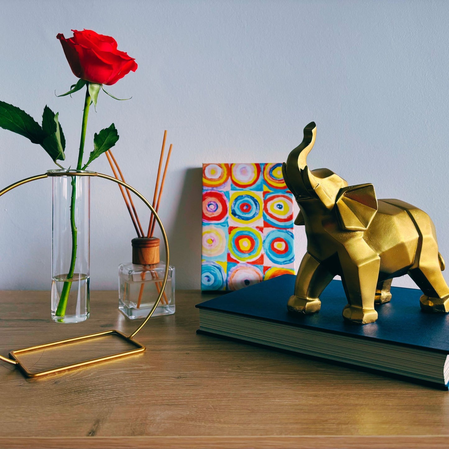 Gold elephant figurine on a book with a red rose and colorful notebook in the background.