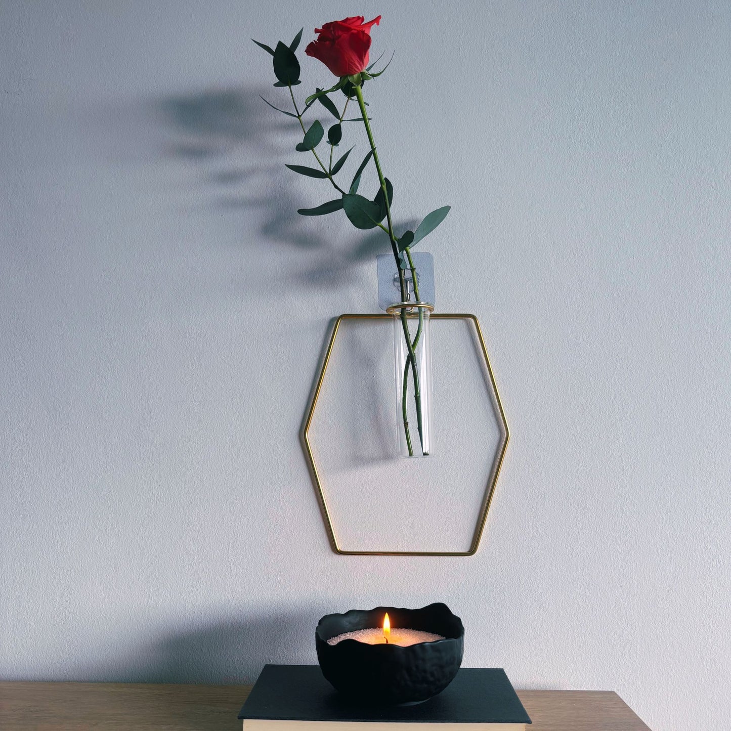 Geometric glass vase with a red rose on a white wall, candle in front