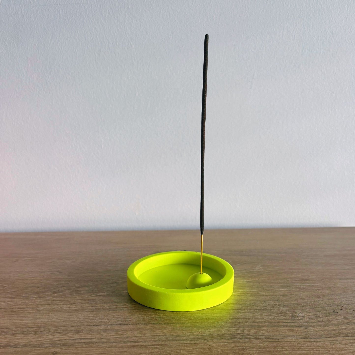 Yellow incense holder with a single black incense stick on a wooden surface.