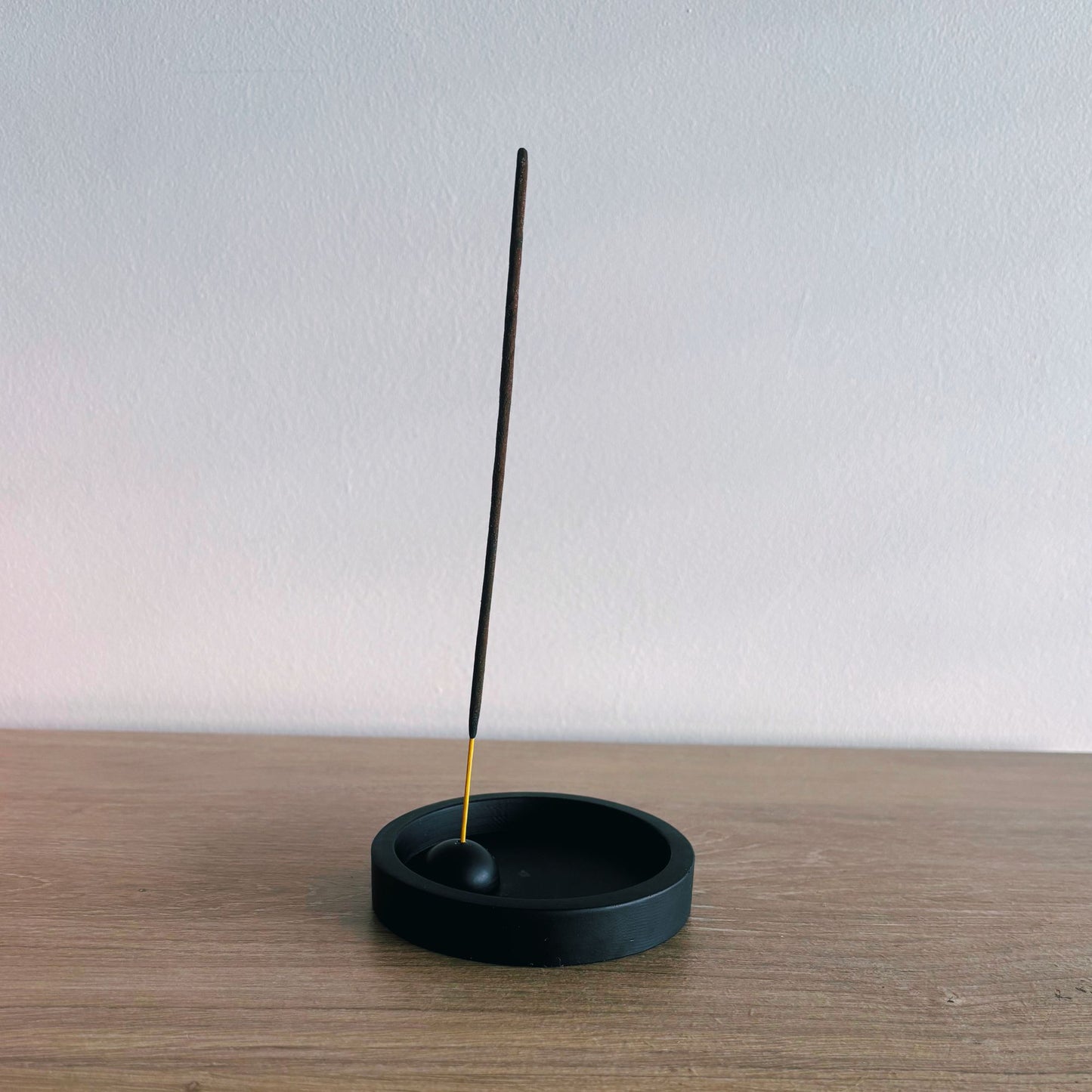 Black incense holder with a single incense stick on a wooden surface.