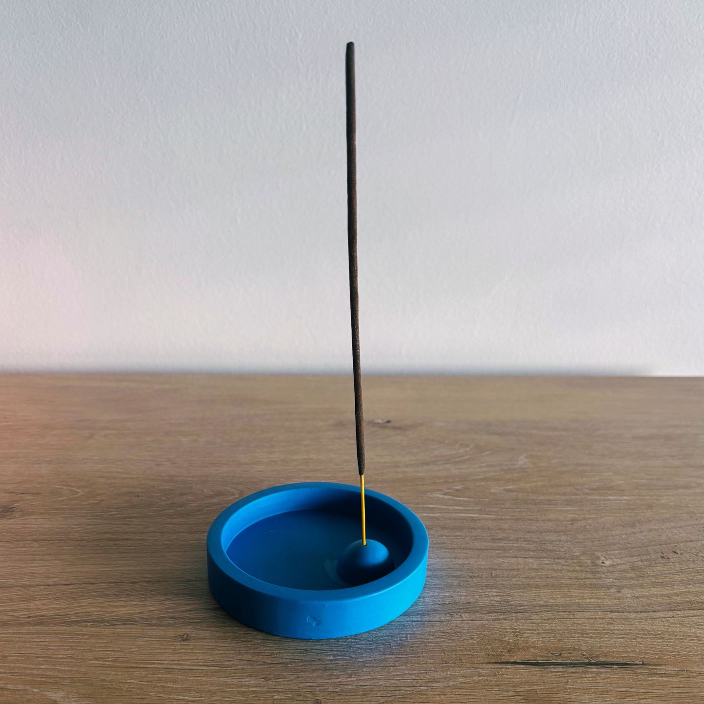 Blue incense holder with a single incense stick on a wooden surface