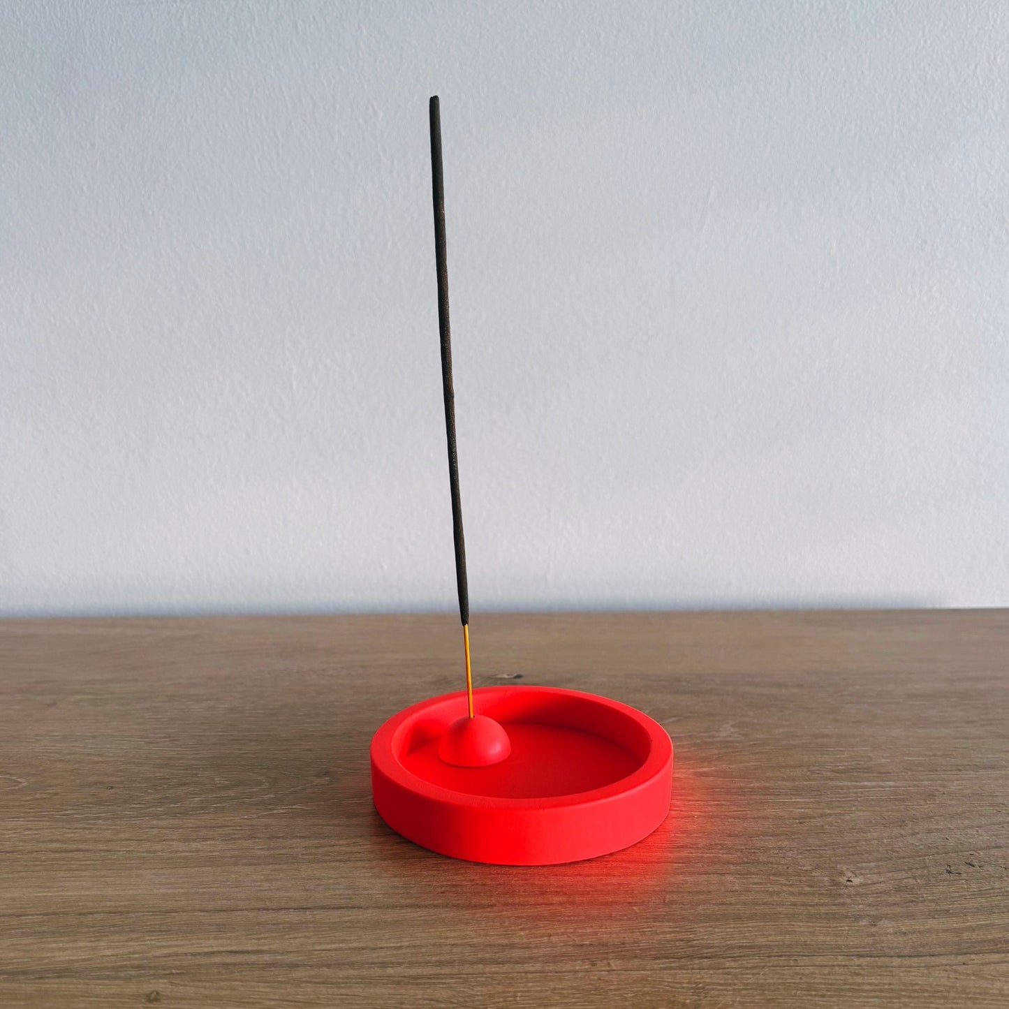 Red incense holder with a single black incense stick on a wooden surface.