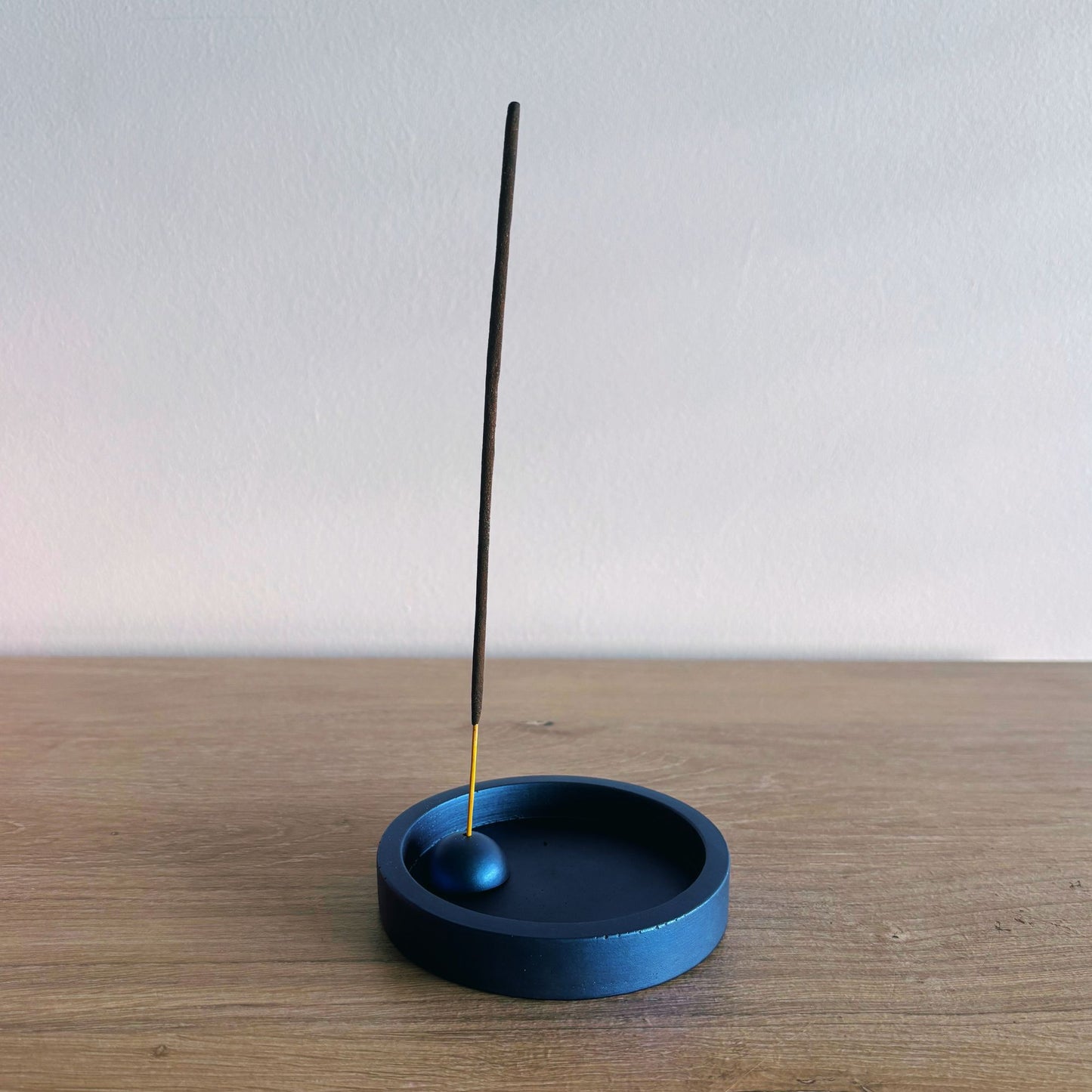 Blue incense holder with a single incense stick on a wooden surface