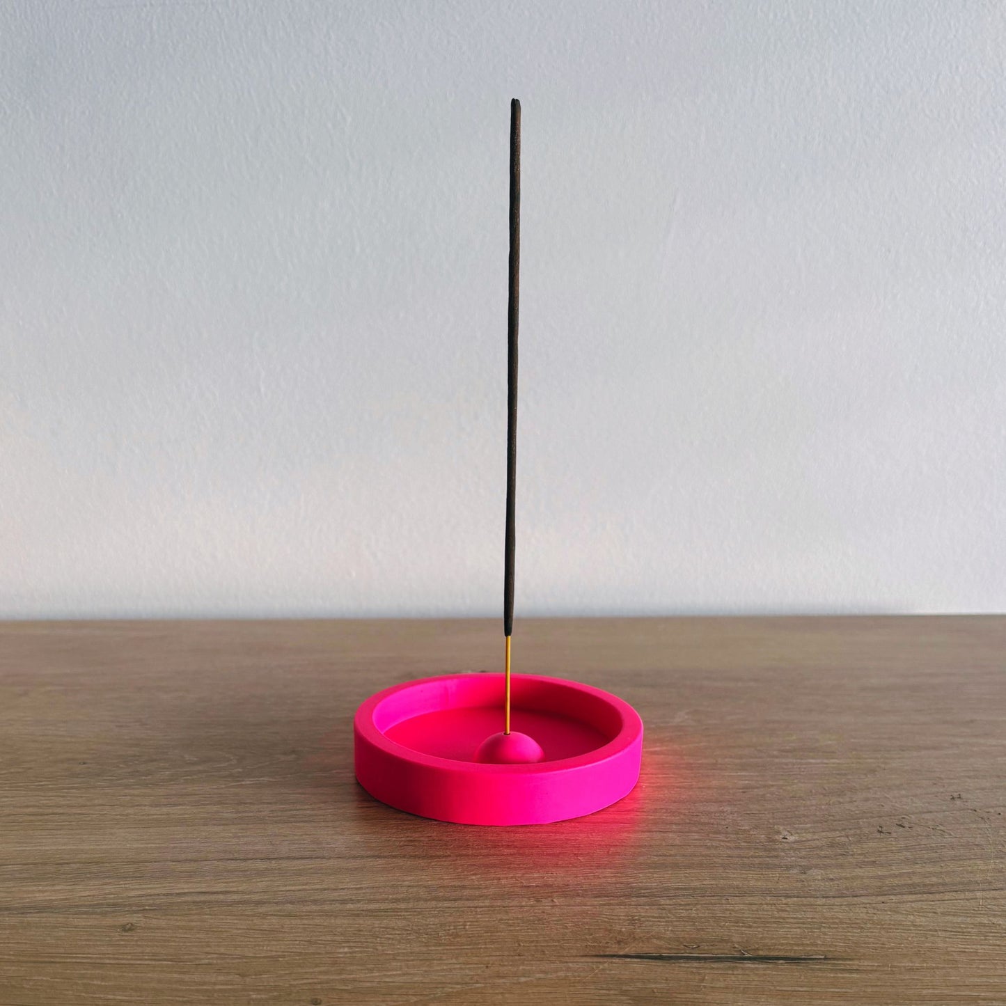 Pink incense holder with a single black incense stick on a wooden surface.
