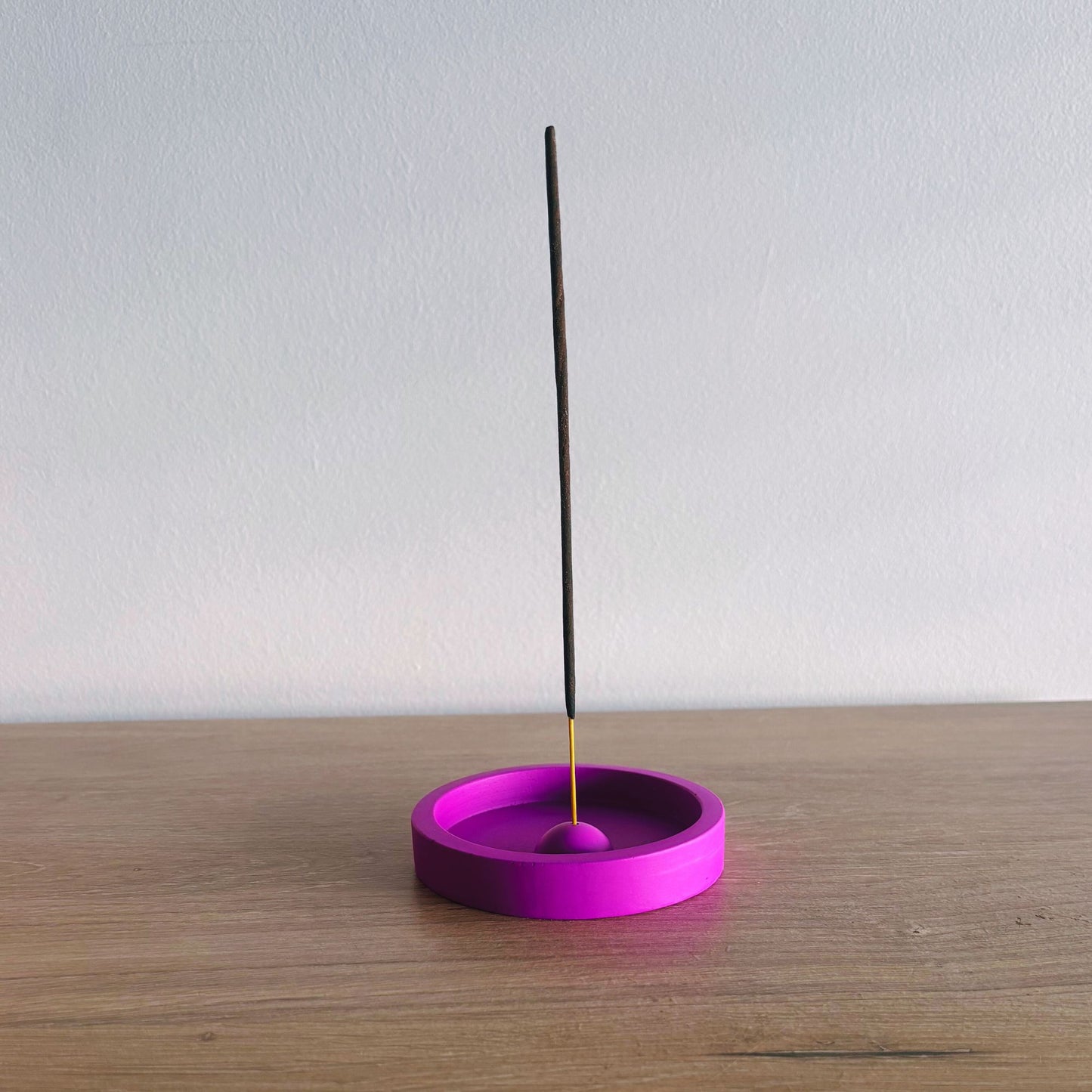Purple incense holder with a single black incense stick on a wooden surface.