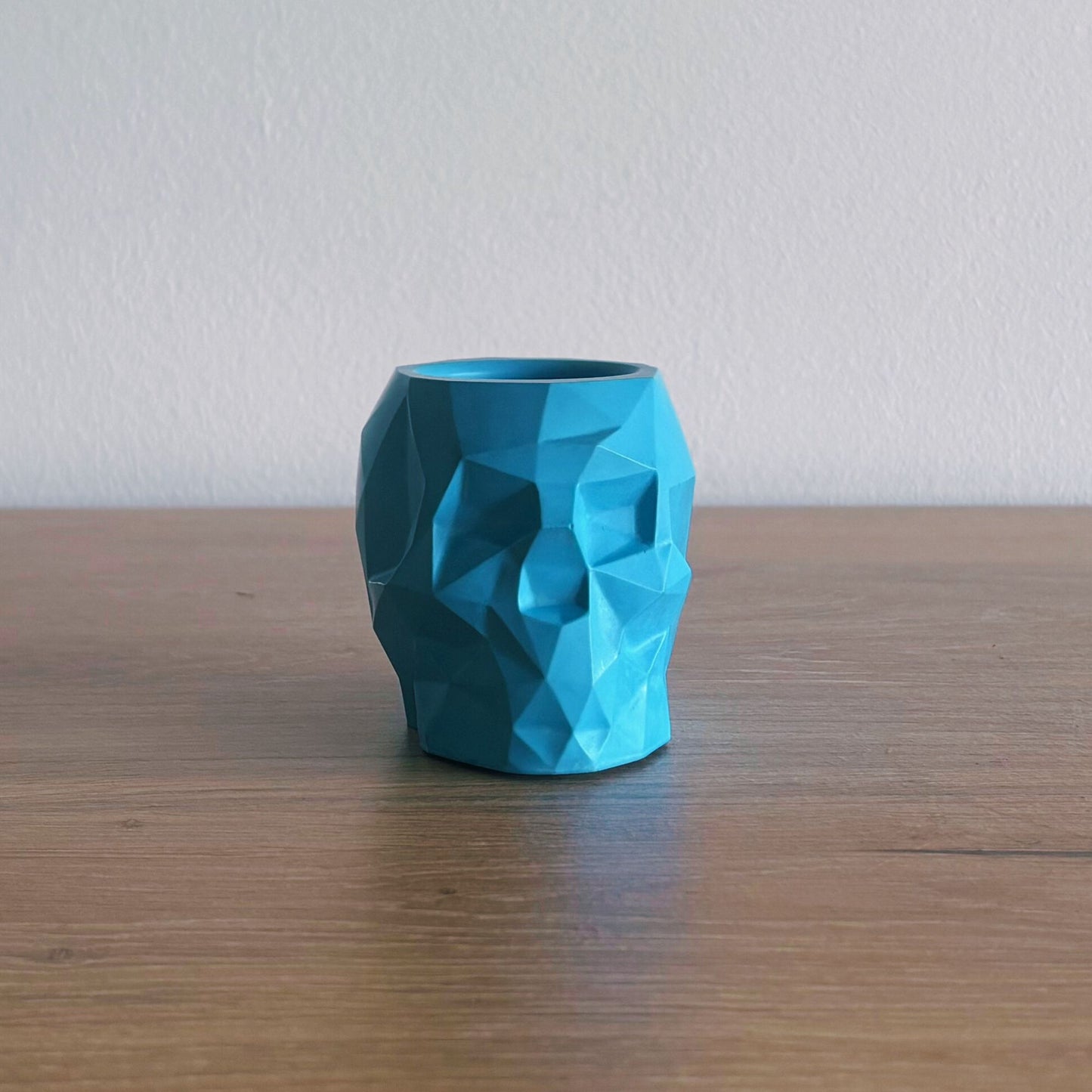 Blue geometric-patterned skull on a wooden surface with a white wall background