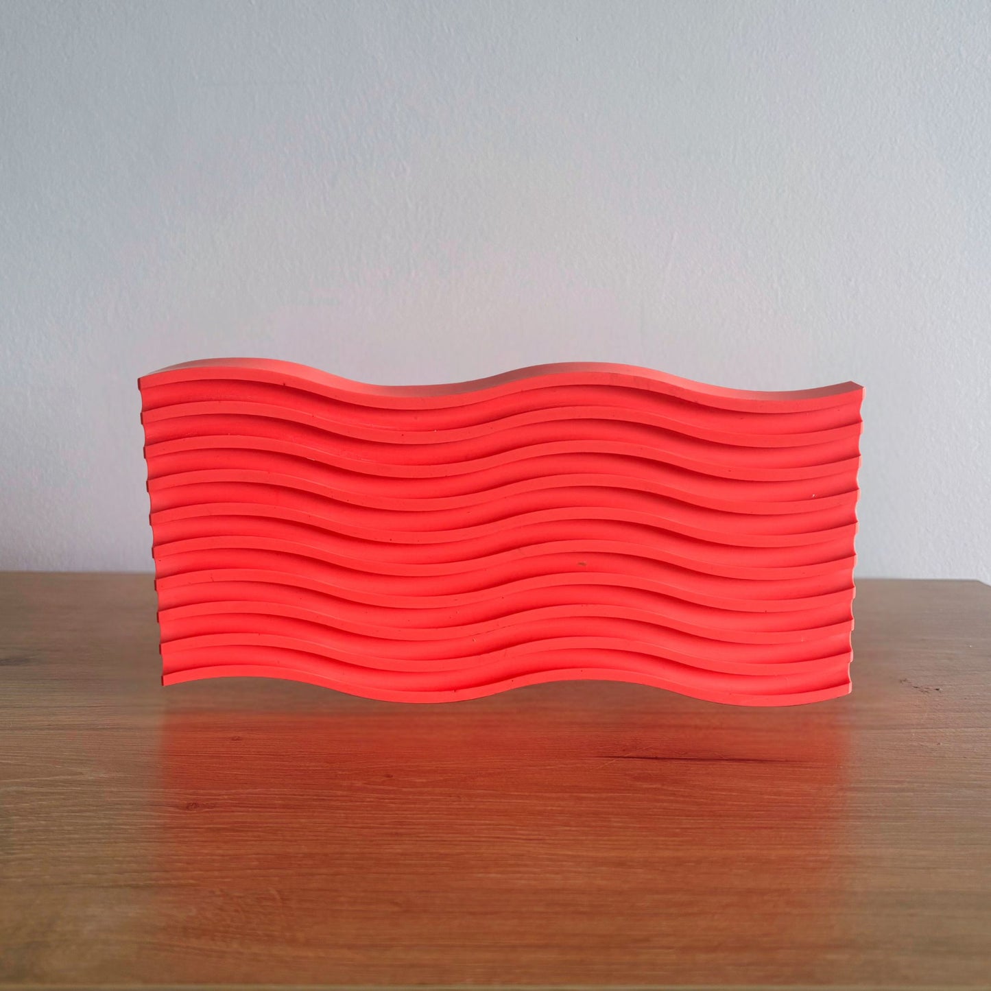 Wave-patterned red object on a wooden surface with a light gray background