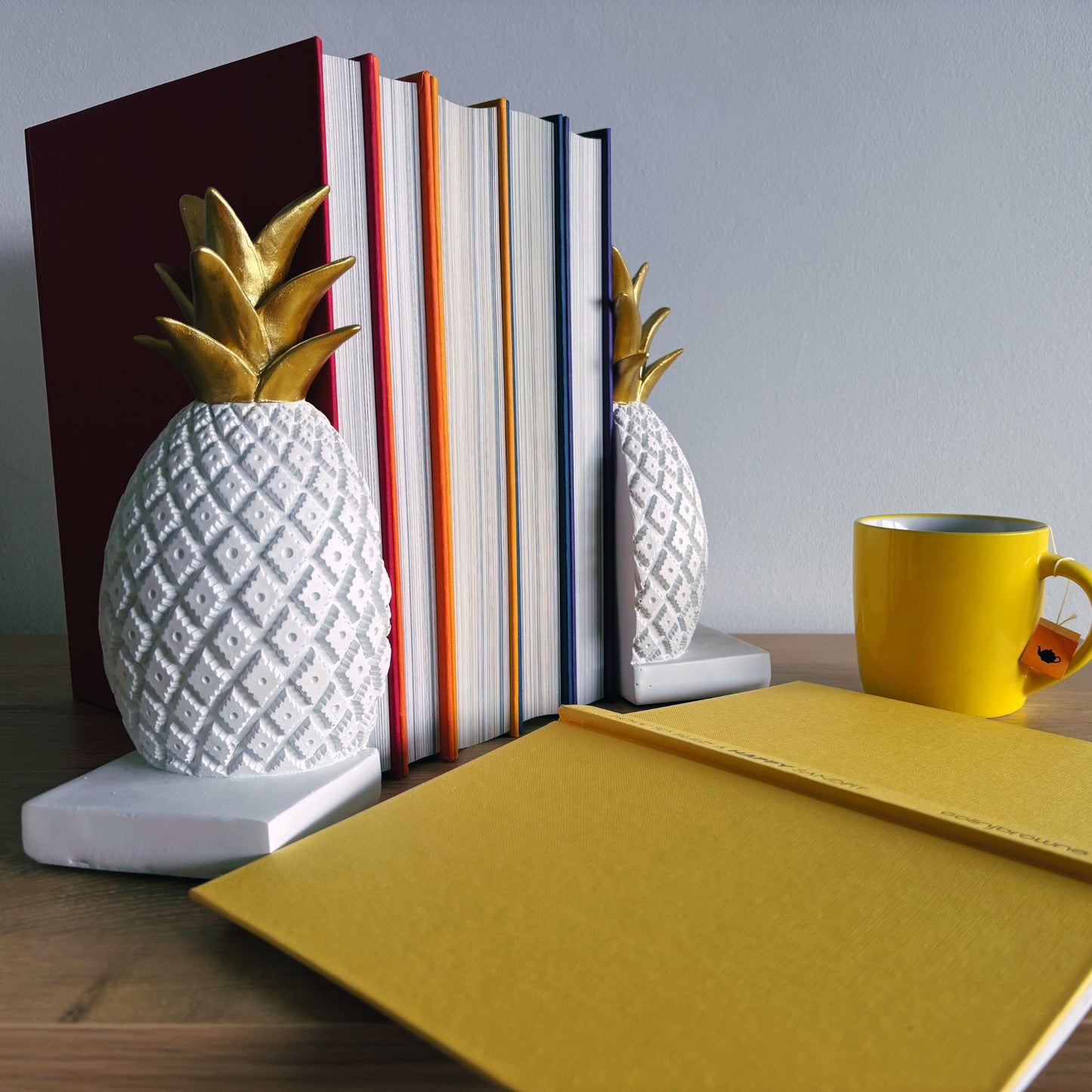 Pineapple-shaped bookends on a shelf with books and a yellow mug.