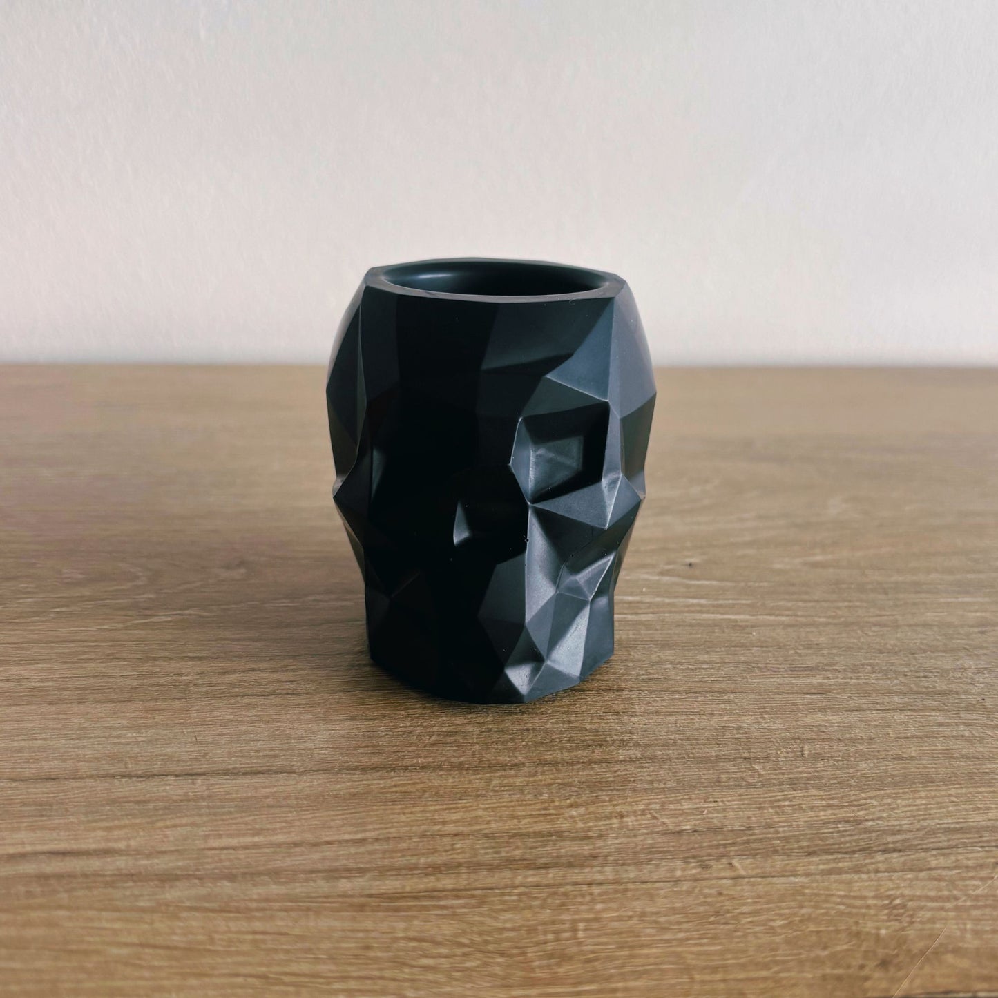 Black geometric-patterned vase on a wooden surface with a plain background