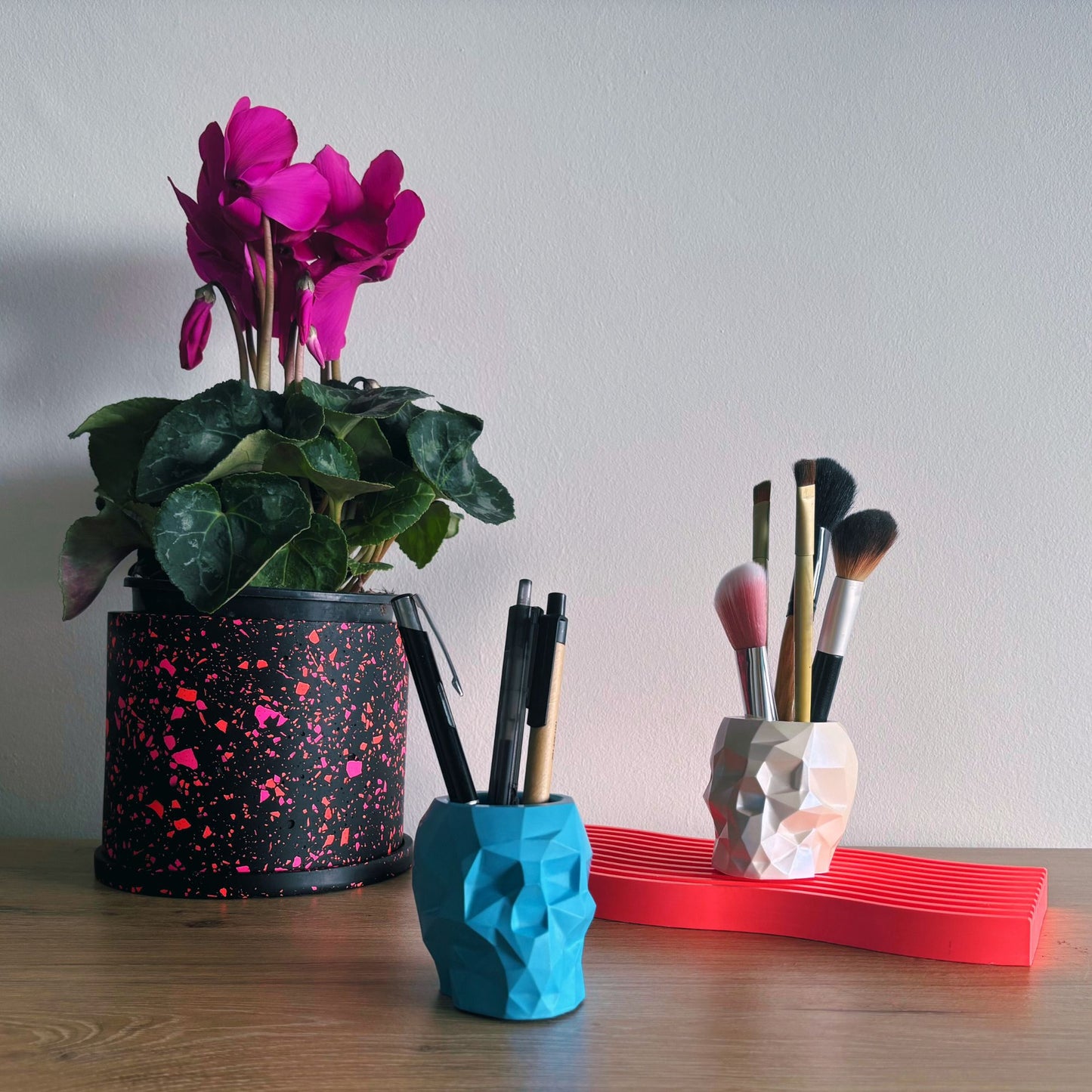 Decorative items including a potted plant, pen holder, and makeup brush holder on a wooden surface.