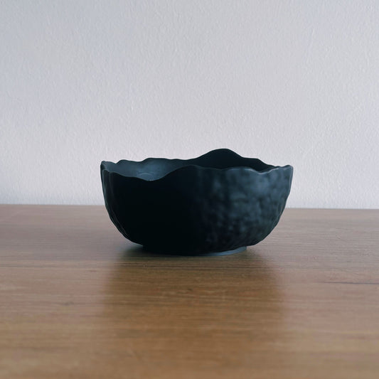 Black ceramic bowl on a wooden surface with a white background