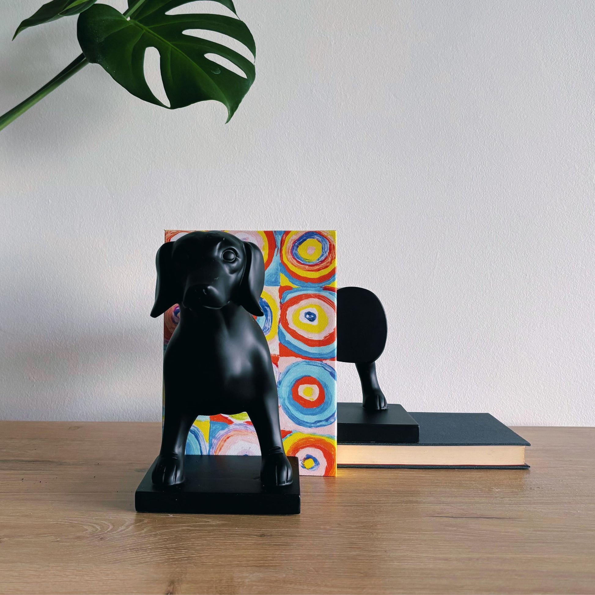 Black dog-shaped bookends on a wooden surface with a colorful book and plant in the background.