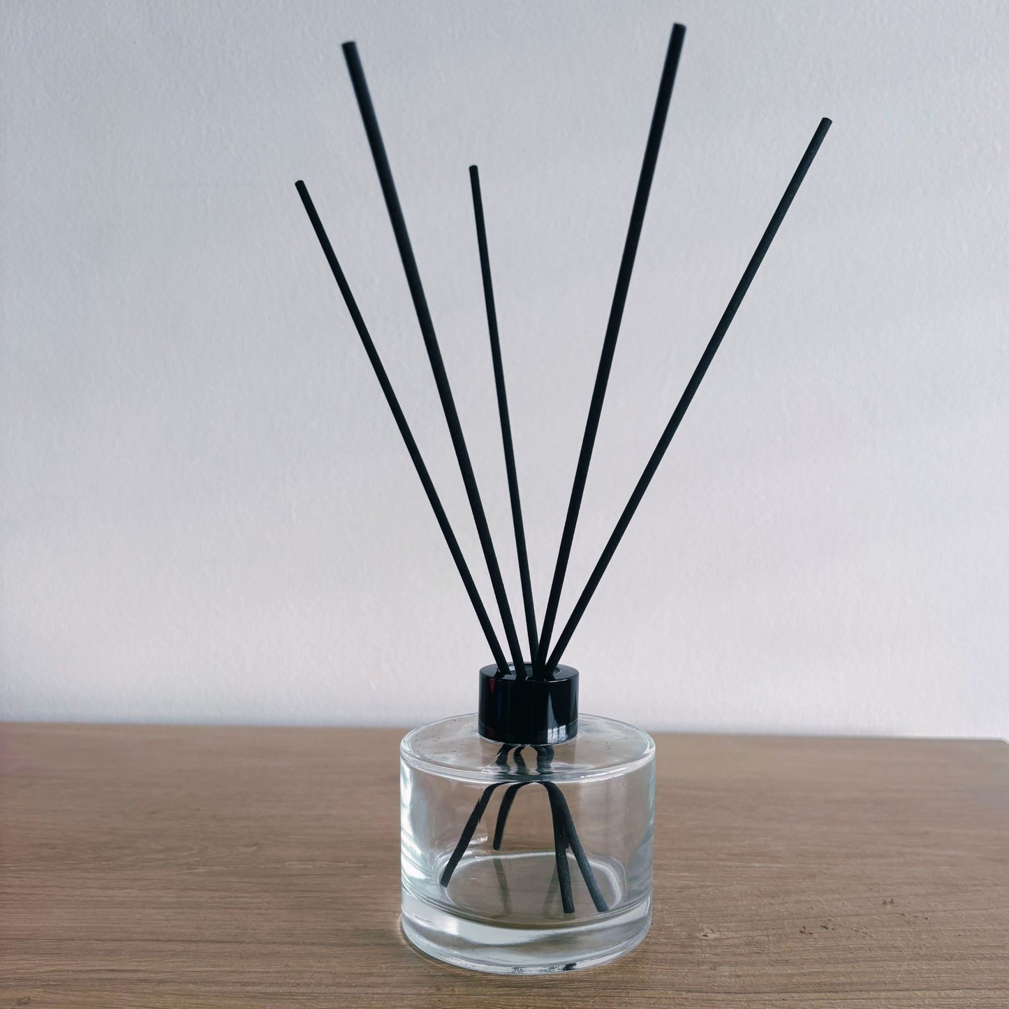 Clear diffuser bottle with black sticks on a wooden surface