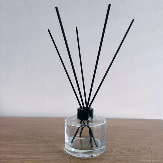 Clear diffuser bottle with black sticks on a wooden surface