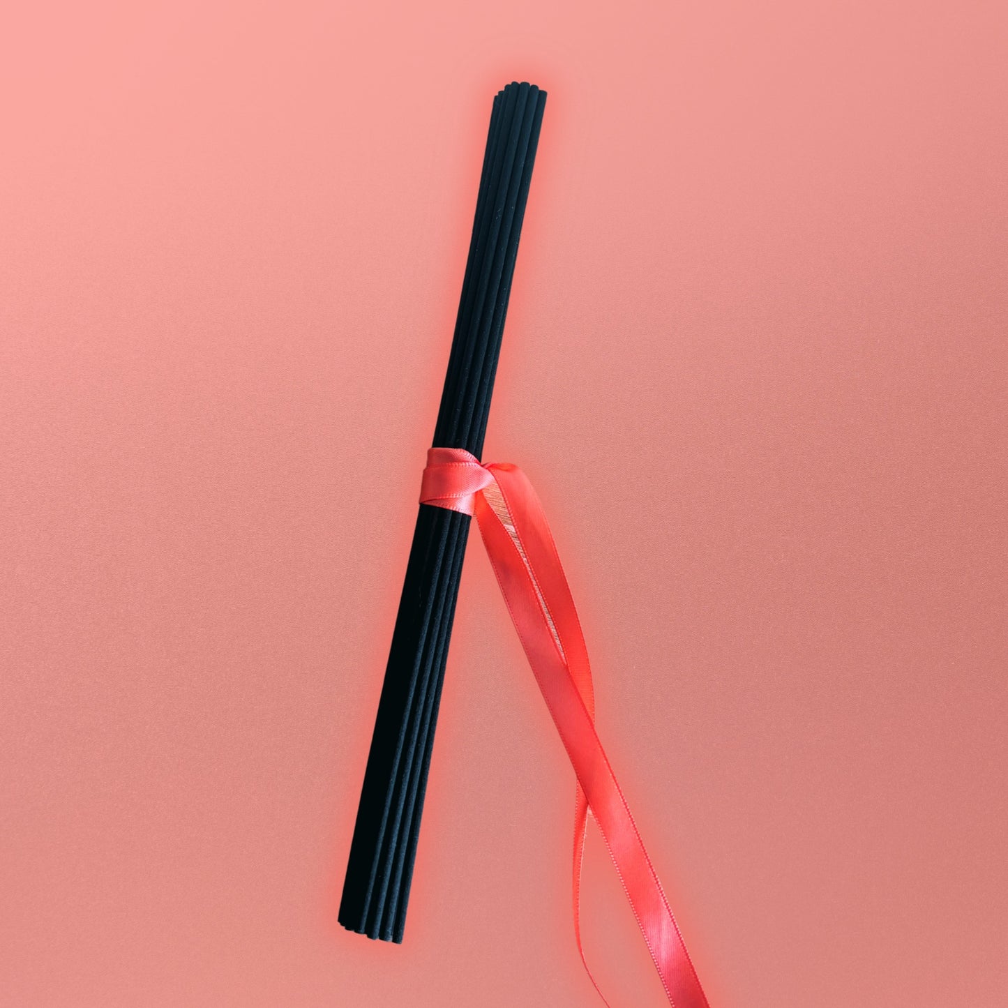 Black diffuser reeds with a red ribbon on a pink background