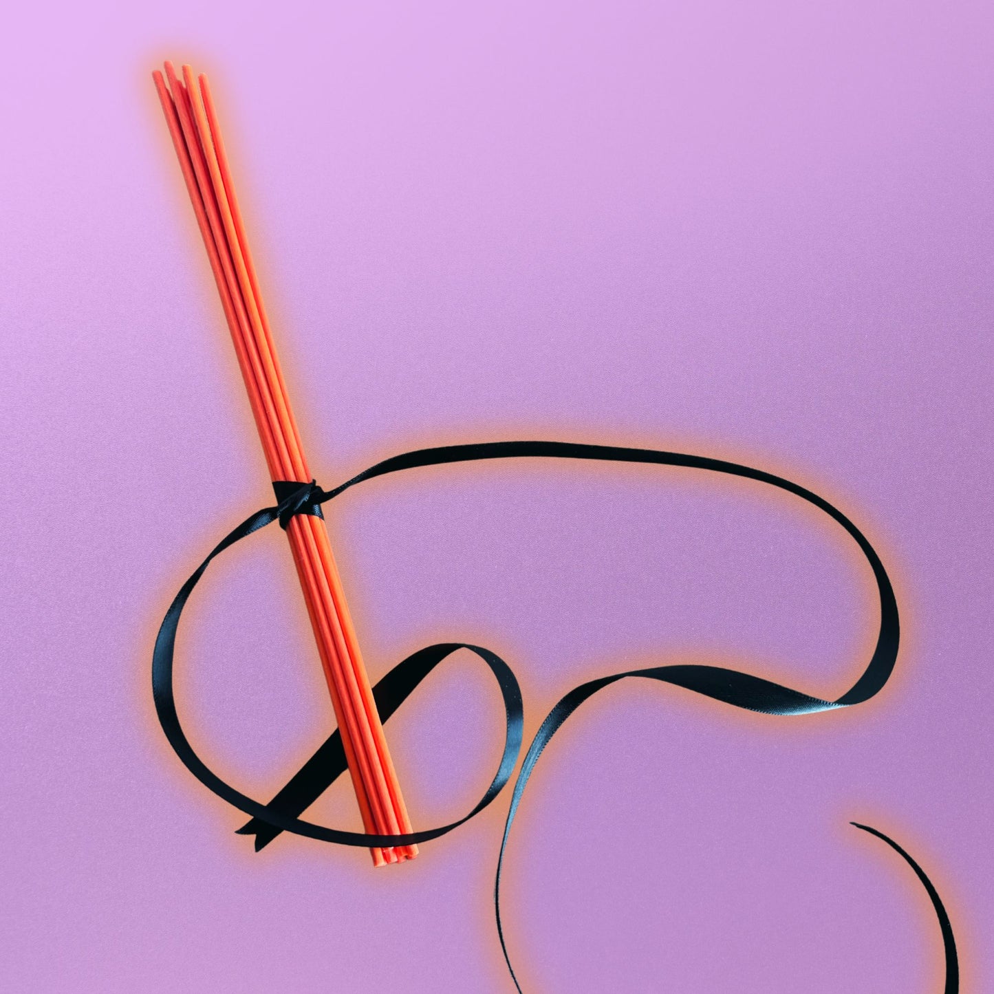 orange diffuser reeds tied with black ribbon on a pink background