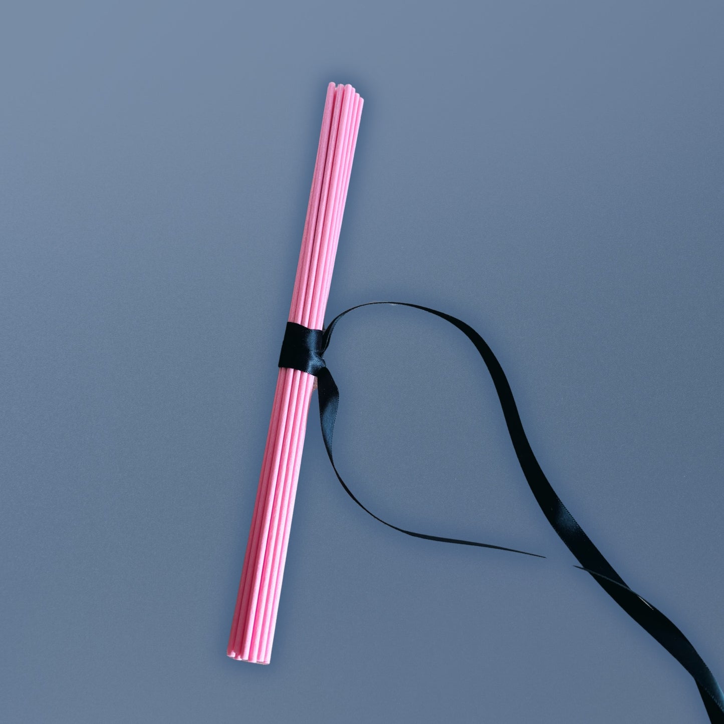 Pink diffuser reeds tied together with a black ribbon on a gray background