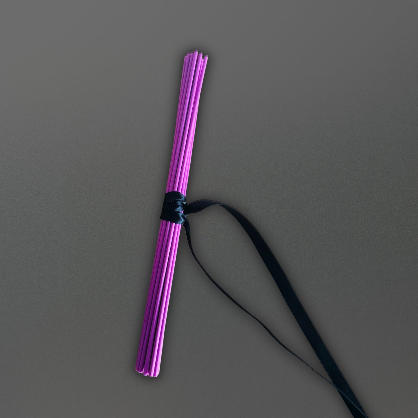 Purple diffuser reeds with black ribbon non a gray background