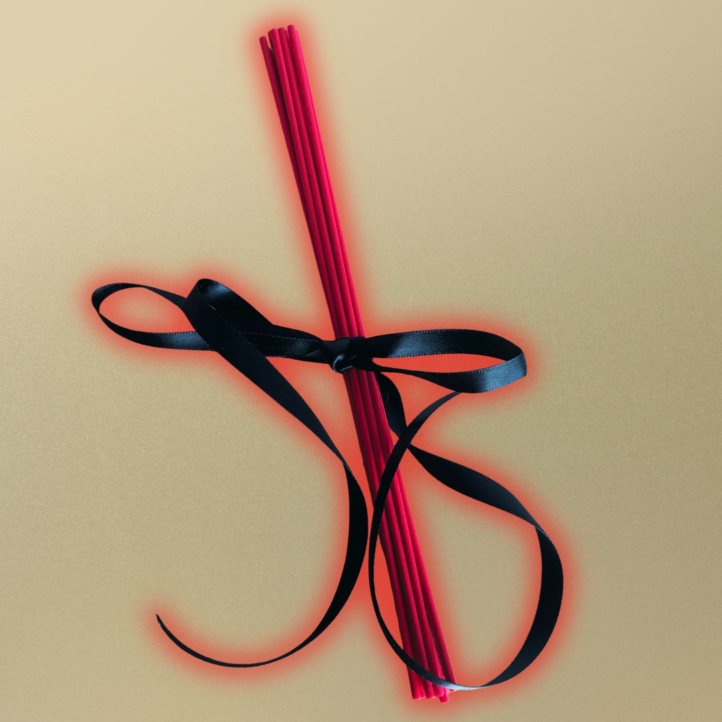 Red diffuser reeds tied with a black ribbon on a beige background