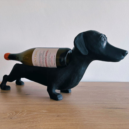 Black dachshund-shaped wine bottle holder with a wine bottle on a wooden surface.