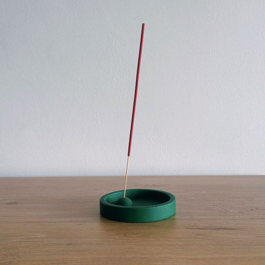 Green incense holder with a single red incense stick on a wooden surface.