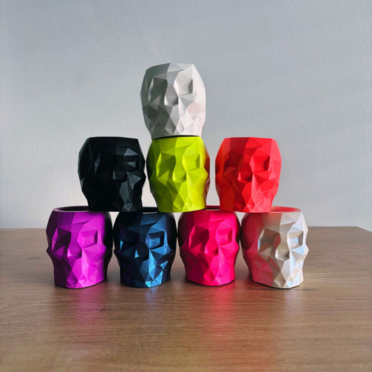 Colorful geometric skull-shaped vases stacked on a wooden surface with a gray background